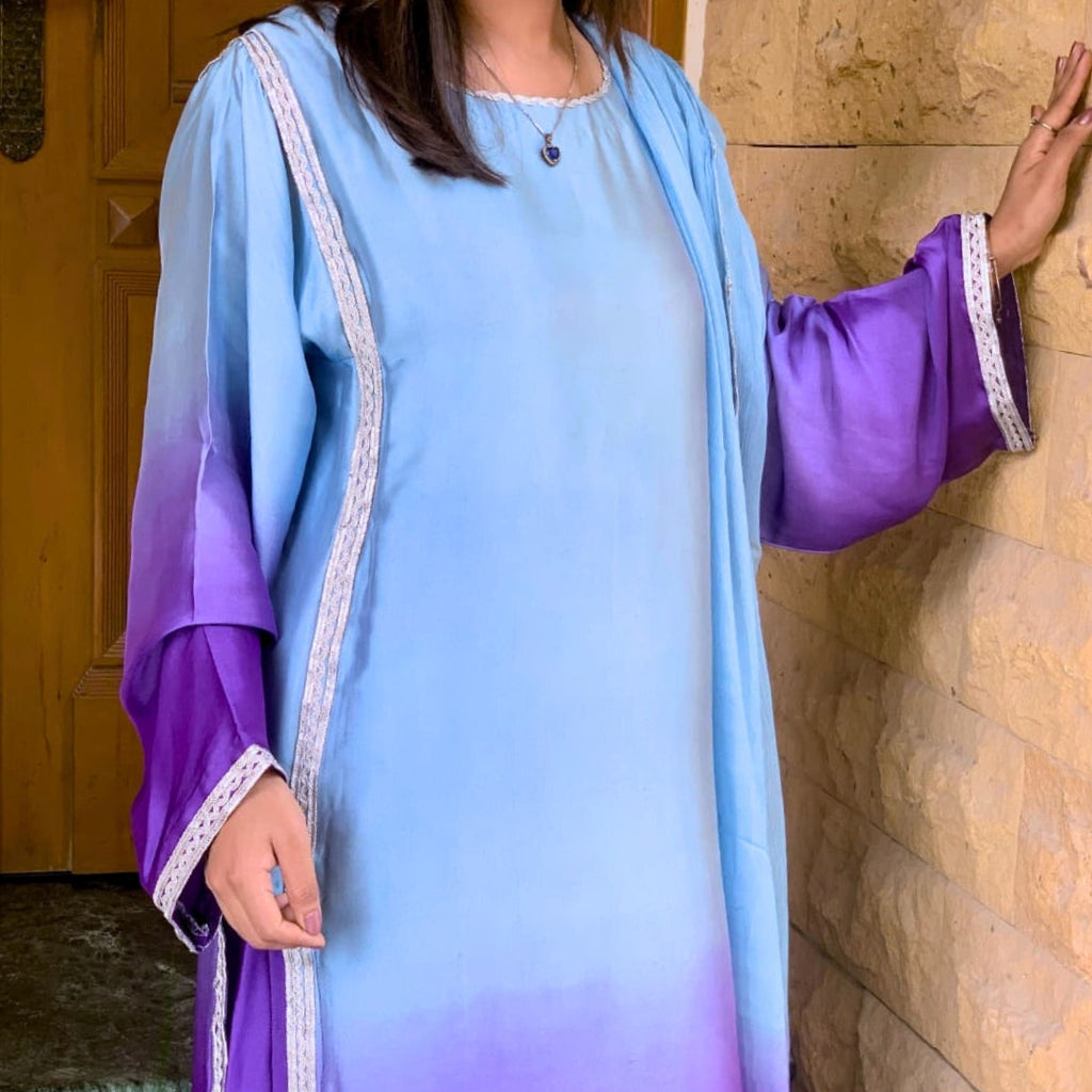 Person wearing a light blue and purple dress with a wooden door and wall in the background