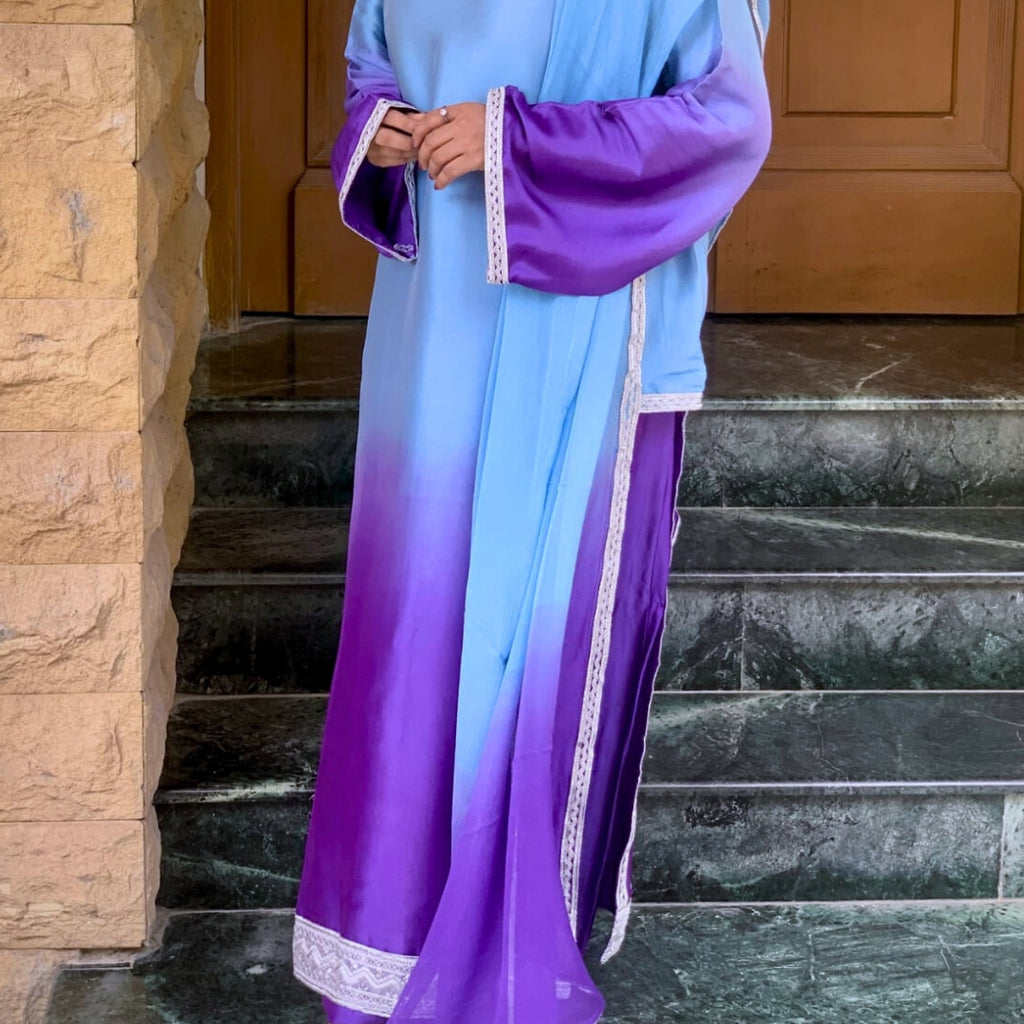 Person wearing a purple and blue gradient dress with white lace trim on stone steps.