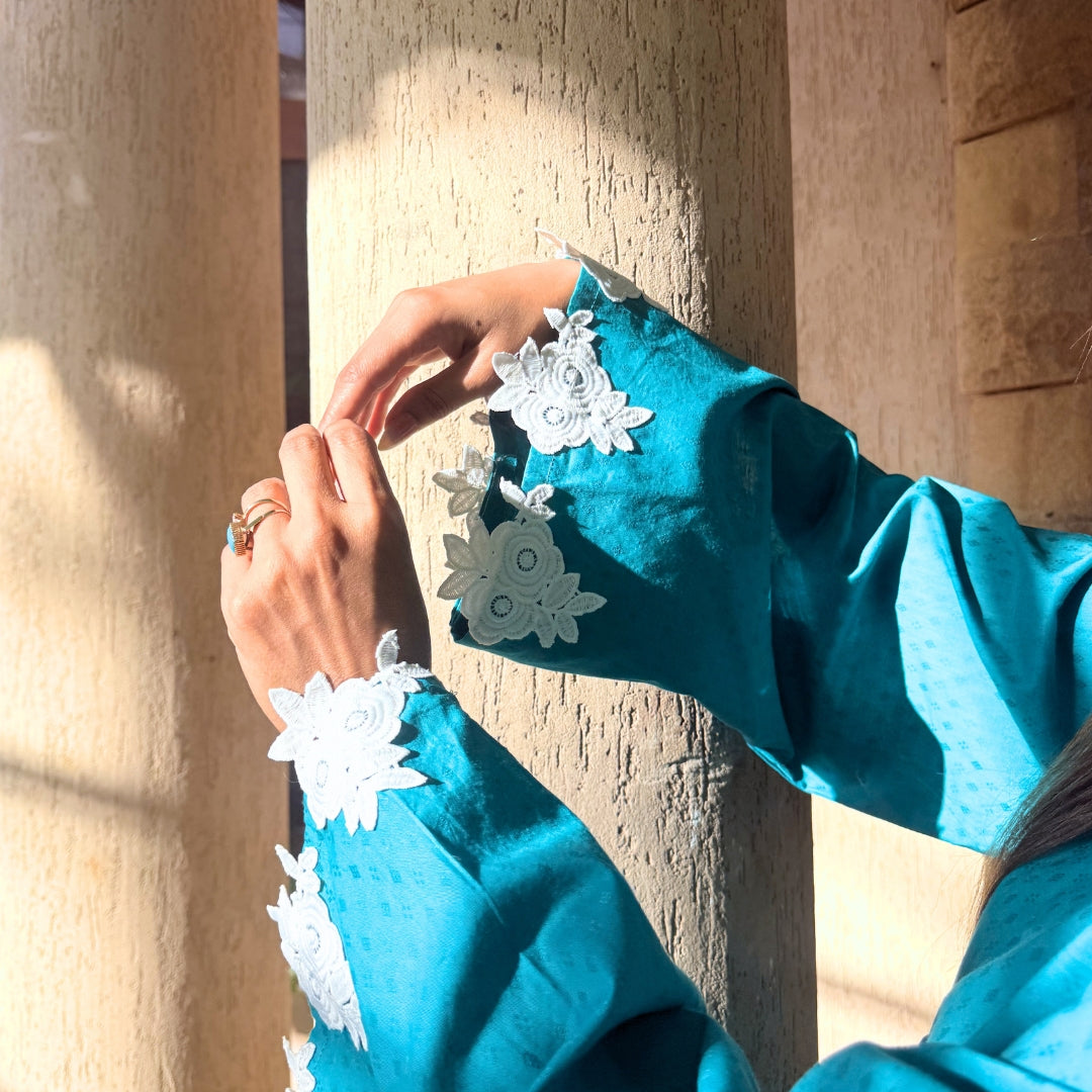 Close-up of a person wearing a blue garment with white floral embroidery against a stone wall.