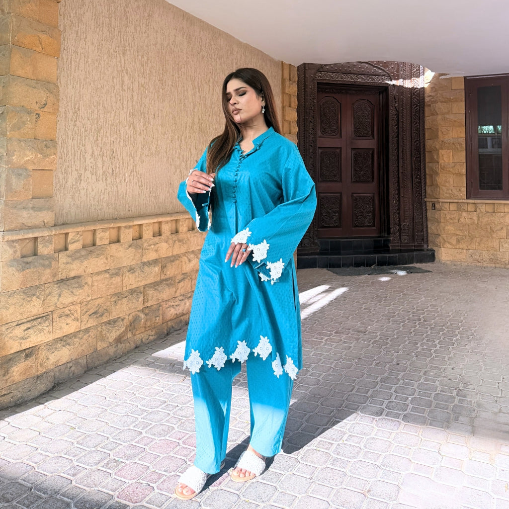 Woman in a blue traditional outfit standing outside a building.