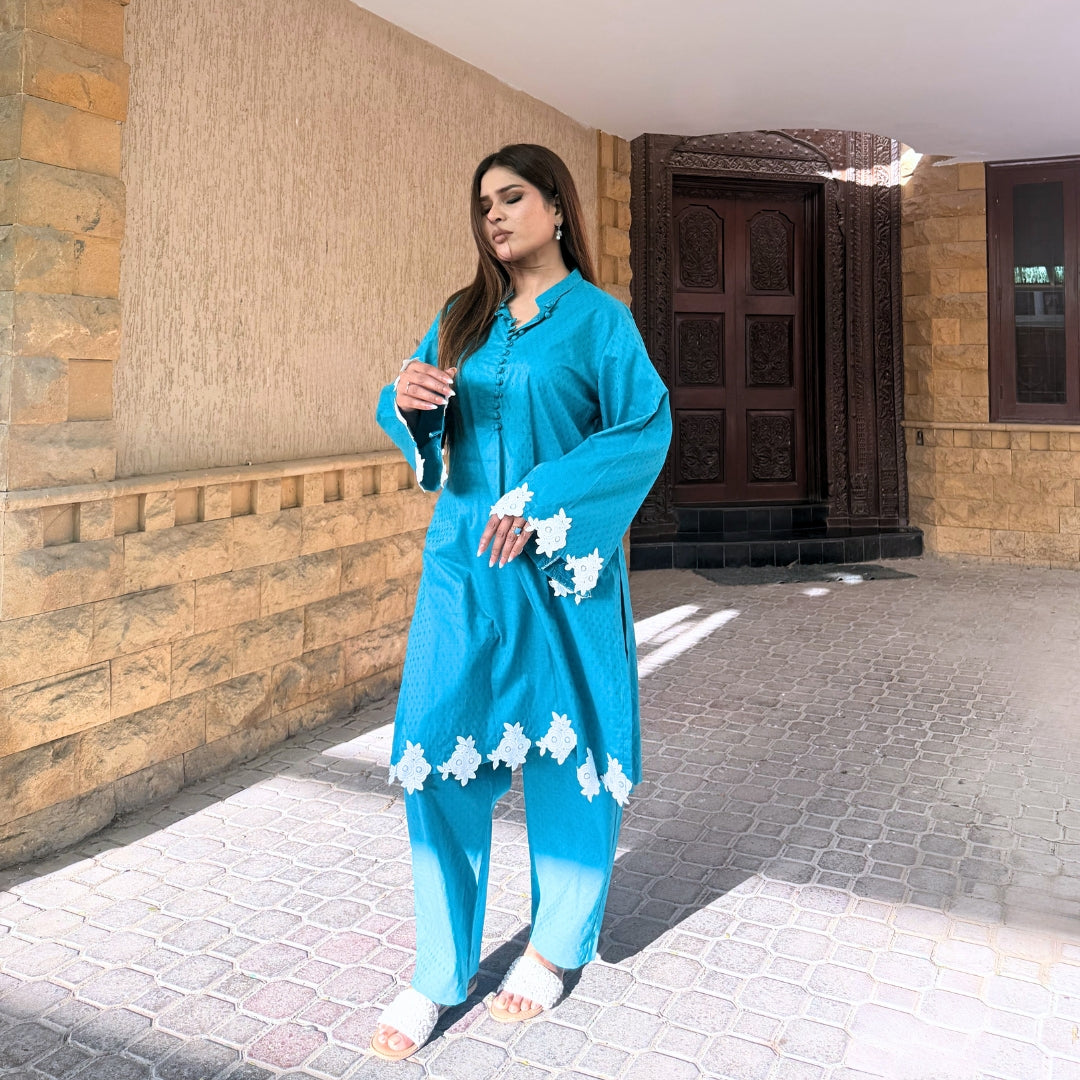 Woman in a blue traditional outfit standing outside a building.