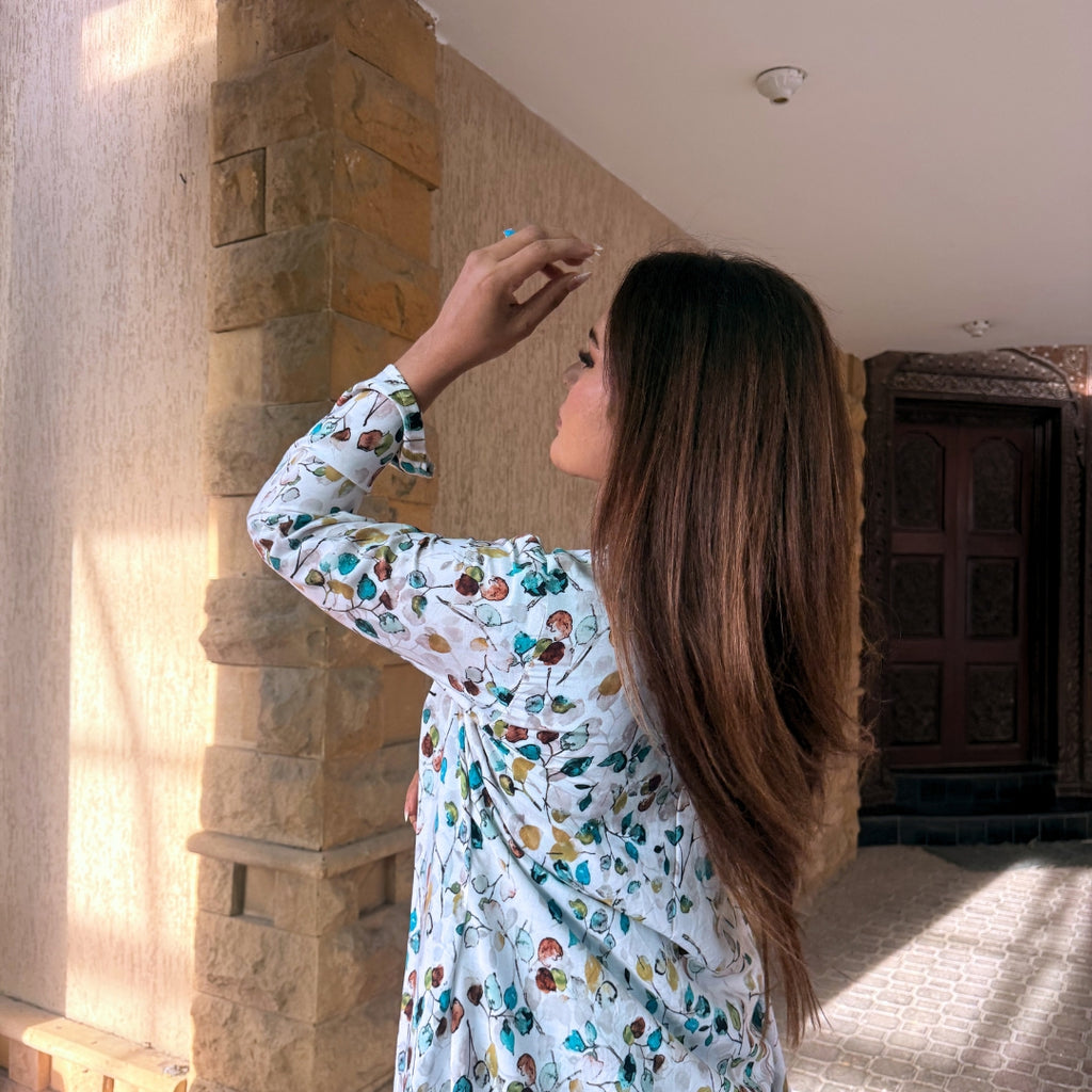Woman in a floral dress standing in a sunlit room with stone walls and wooden doors.