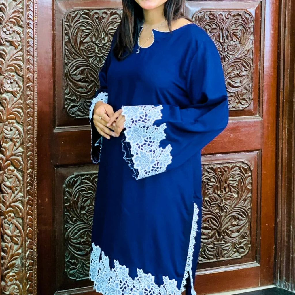 Woman wearing a blue dress with white lace details in front of a wooden door.