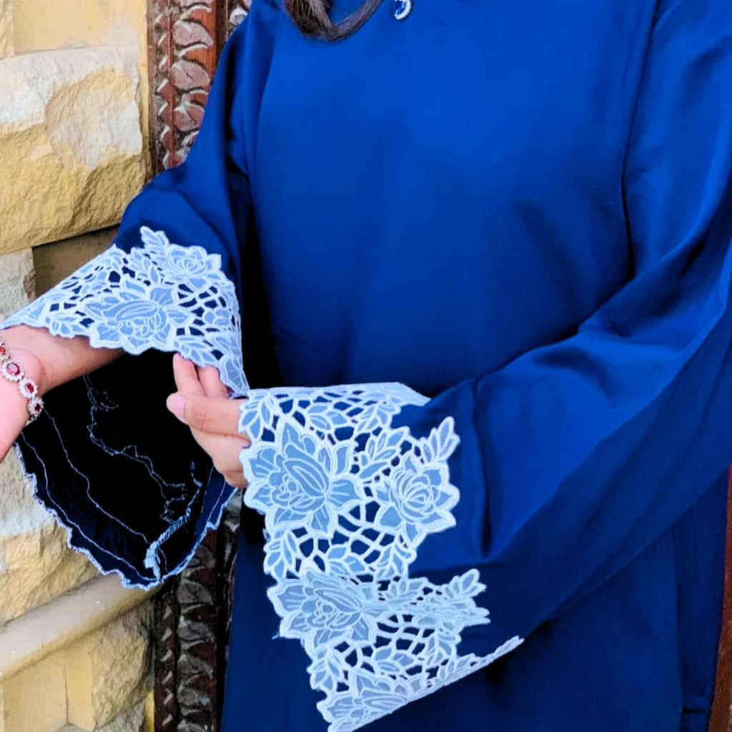Blue garment with white lace details held by a person against a stone wall.