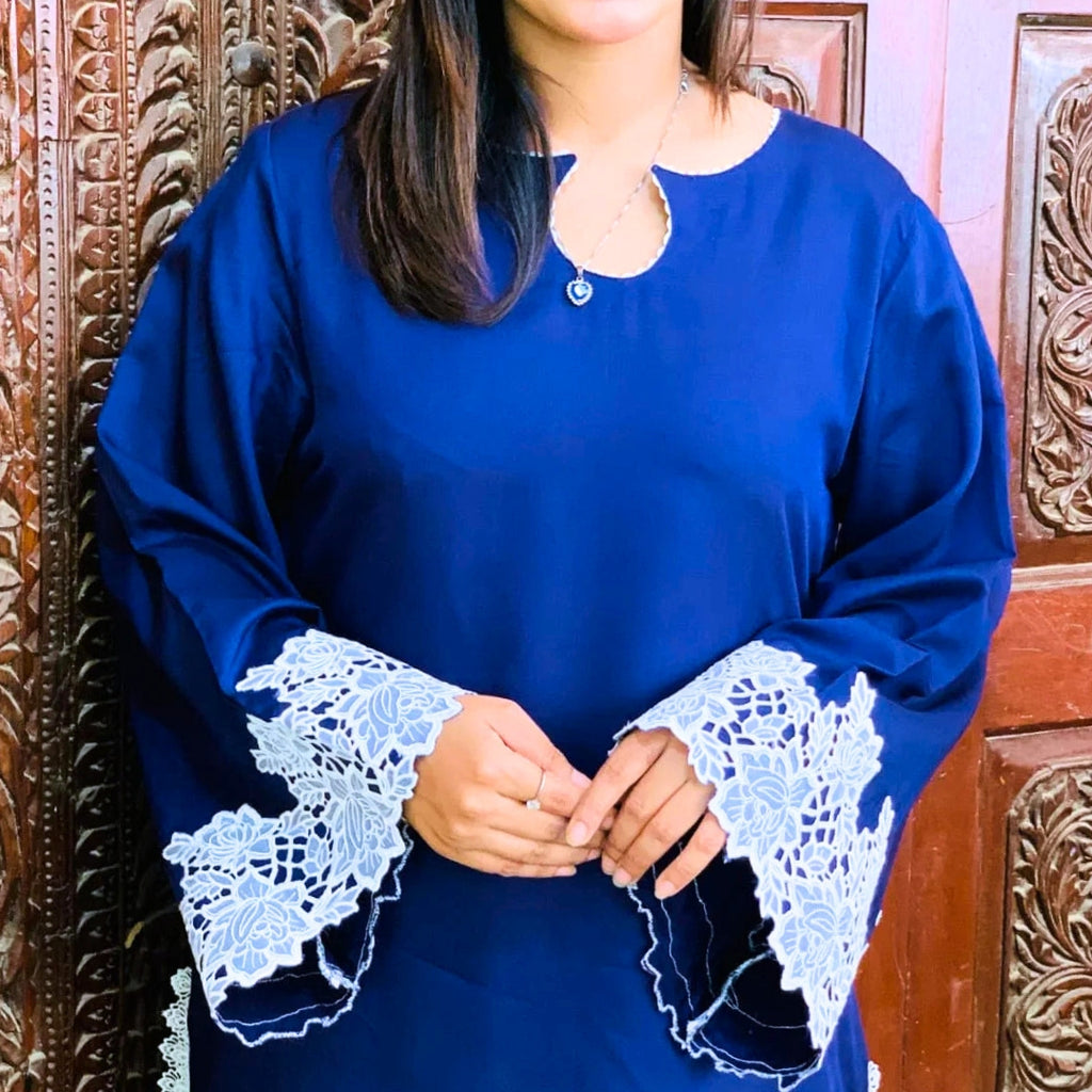 Person wearing a blue dress with lace sleeves against an ornate wooden background