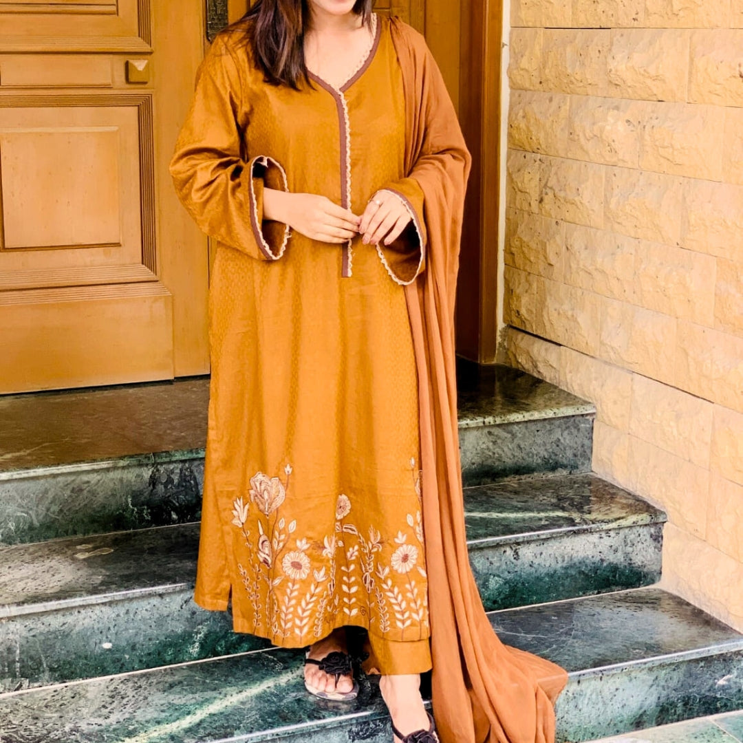 Woman in a mustard yellow traditional outfit with floral patterns standing on stone steps.