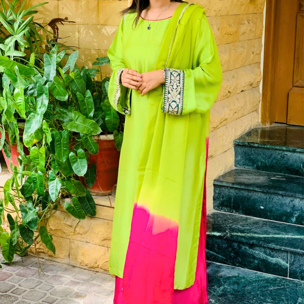 Person wearing a bright green and pink outfit standing outdoors with plants and steps in the background