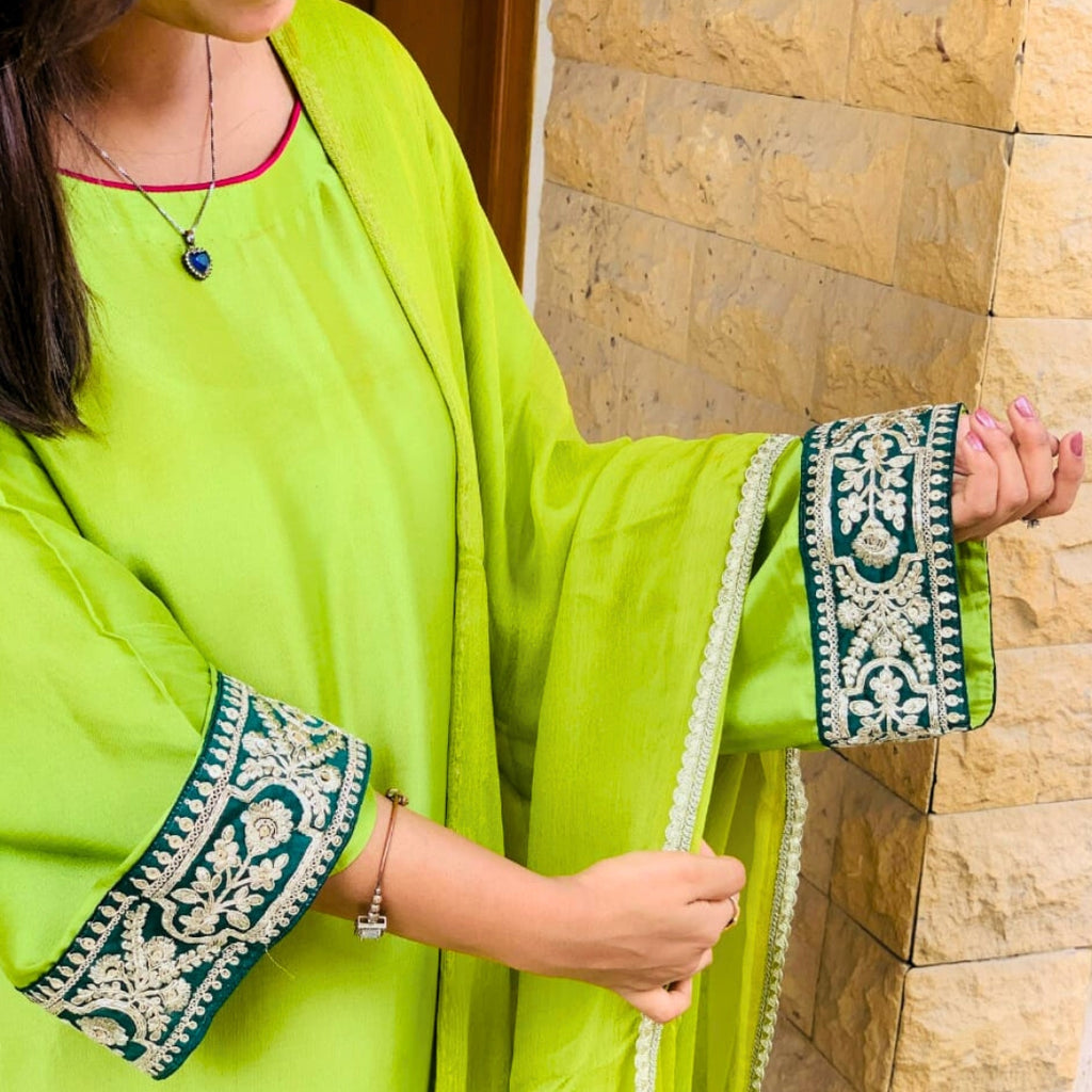 Person wearing a bright green outfit with intricate patterns, standing against a stone wall.