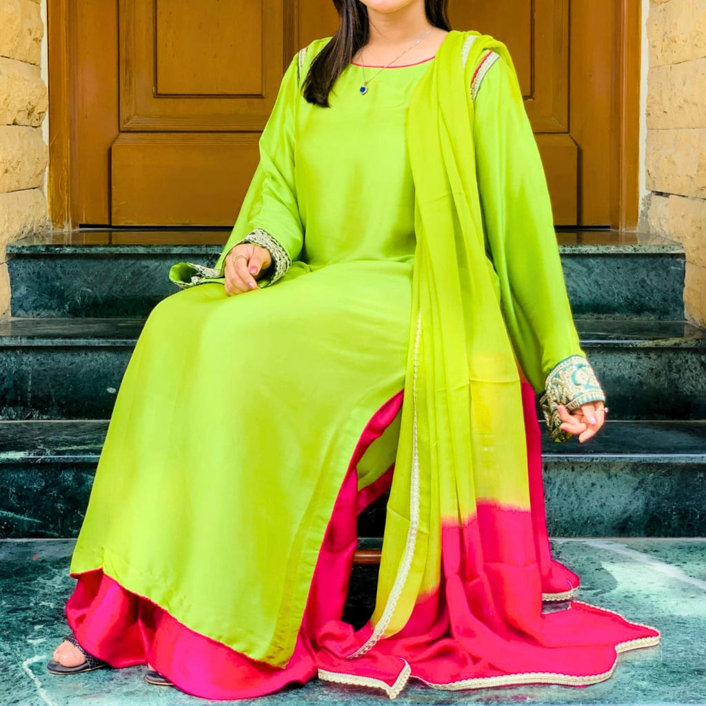 Person wearing a bright green and pink traditional outfit sitting on steps.