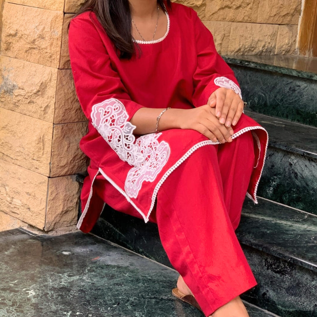 Person wearing a red outfit with white lace details sitting on steps.
