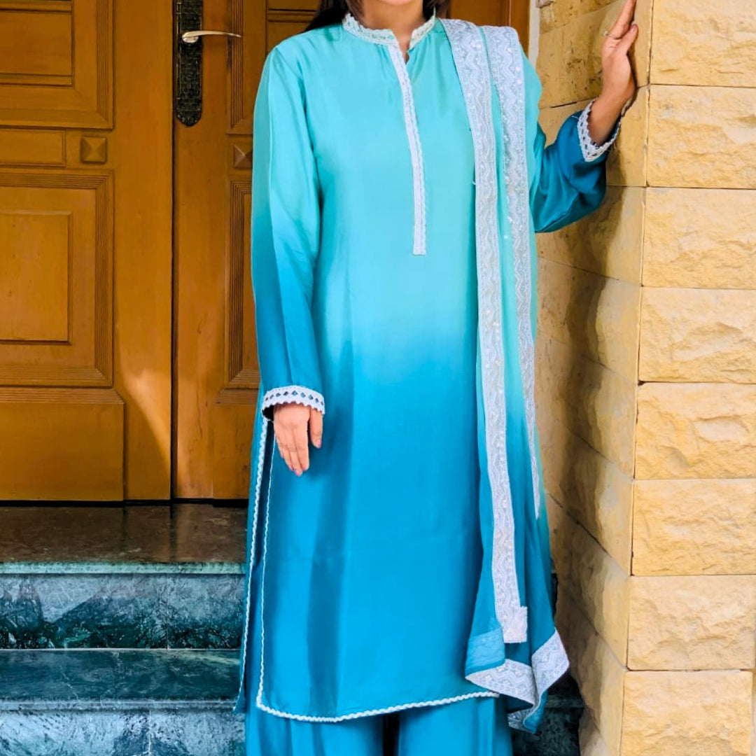 Person wearing a blue traditional outfit with a matching dupatta, standing against a stone wall.