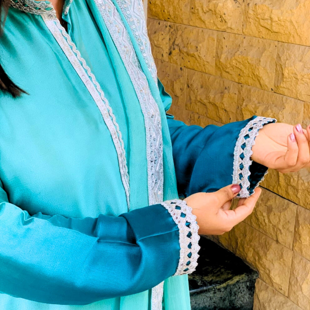 Person wearing a turquoise outfit with lace details against a wooden wall.