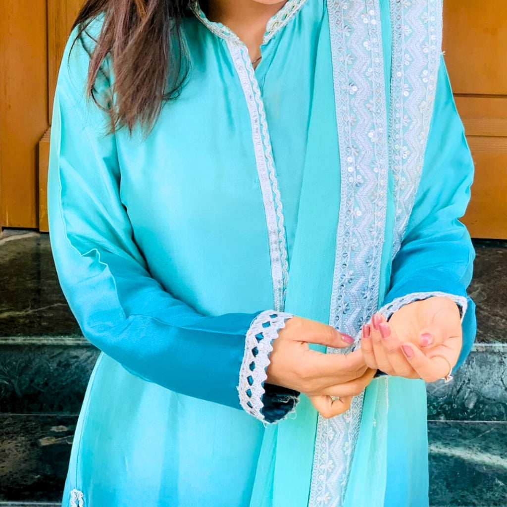 Person wearing a light blue traditional outfit with white lace details.