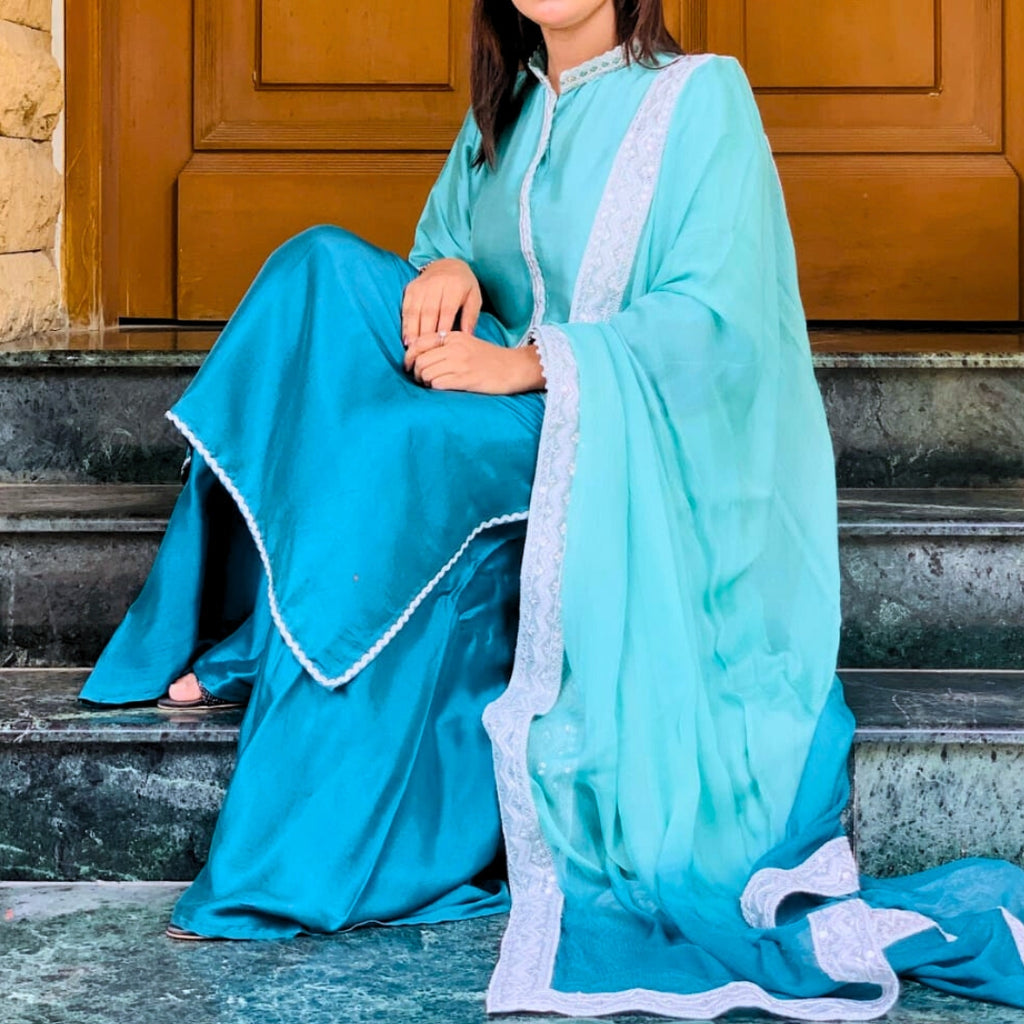 Woman in a turquoise traditional outfit sitting on steps.