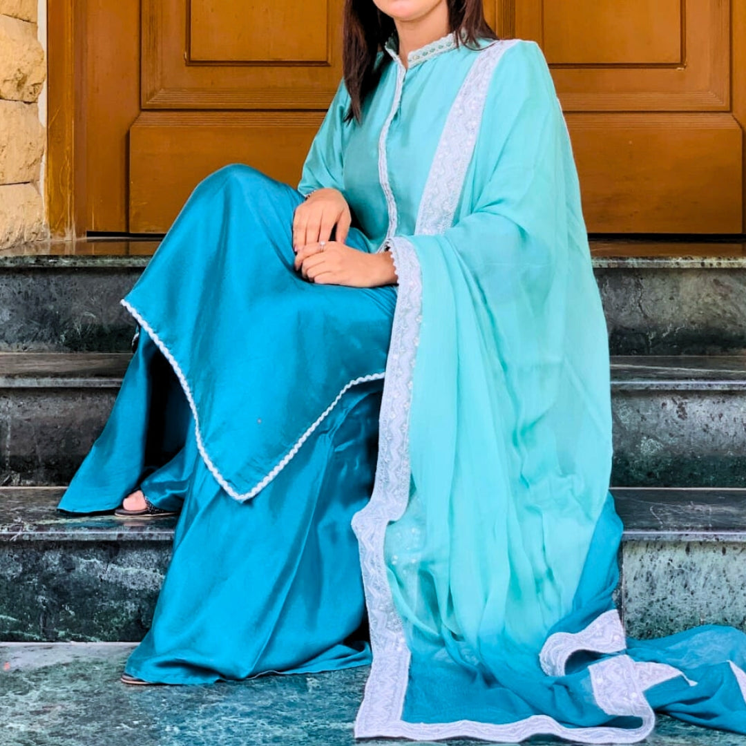 Woman in a turquoise traditional outfit sitting on steps.