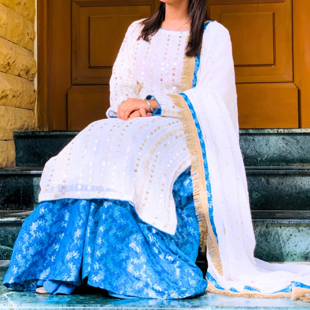 Woman in a white and blue traditional outfit sitting on steps.