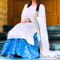 Woman in a white and blue traditional outfit sitting on steps.